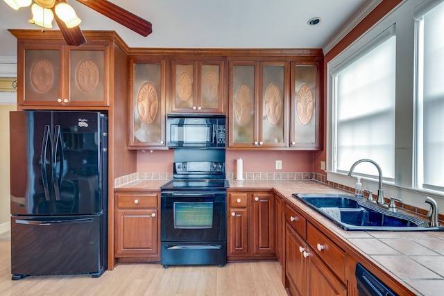 kitchen featuring sink, tile counters, ceiling fan, black appliances, and light wood-type flooring