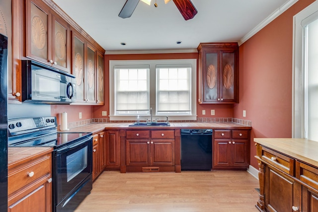 kitchen featuring sink, crown molding, light hardwood / wood-style flooring, tile counters, and black appliances