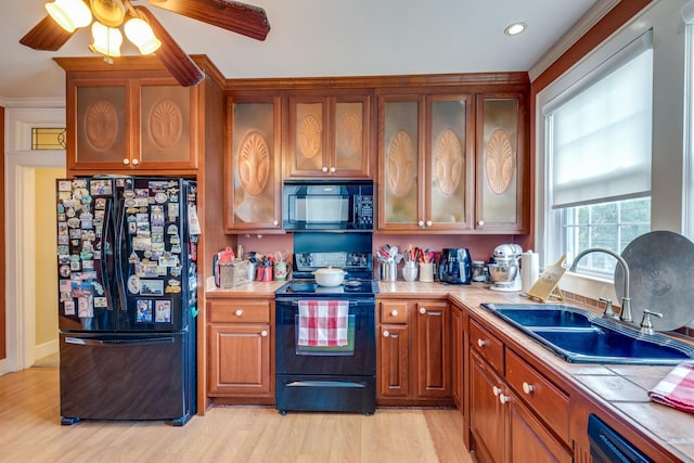 kitchen with sink, light wood-type flooring, tile counters, ceiling fan, and black appliances