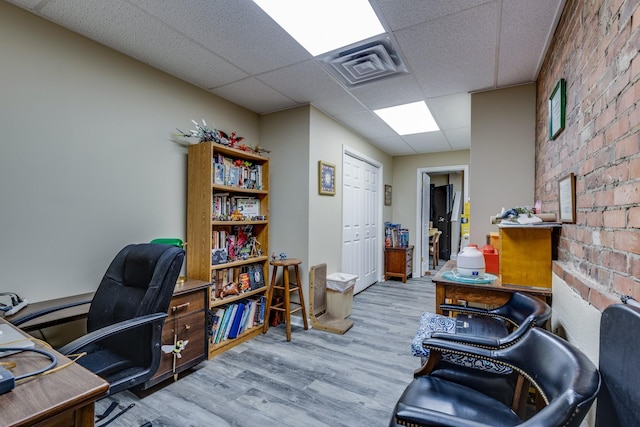 home office featuring brick wall, light hardwood / wood-style floors, and a drop ceiling