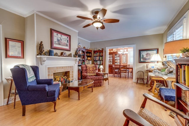 living area featuring crown molding, ceiling fan with notable chandelier, a fireplace, and light hardwood / wood-style floors