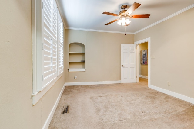 carpeted spare room with built in shelves, ornamental molding, and ceiling fan