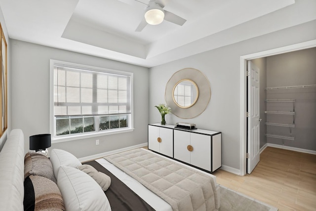 bedroom featuring a raised ceiling, ceiling fan, a spacious closet, and light wood-type flooring