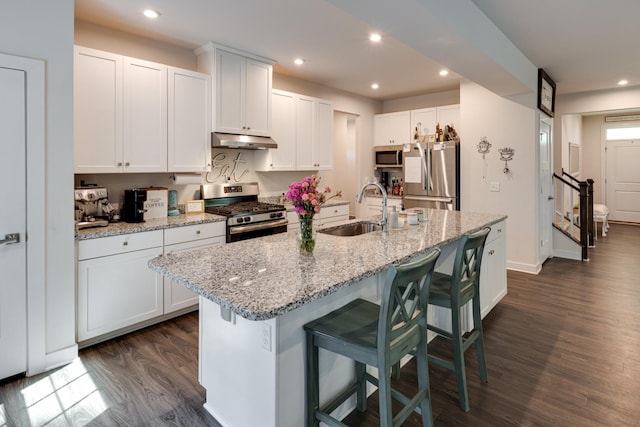 kitchen with appliances with stainless steel finishes, white cabinetry, sink, a kitchen island with sink, and light stone counters