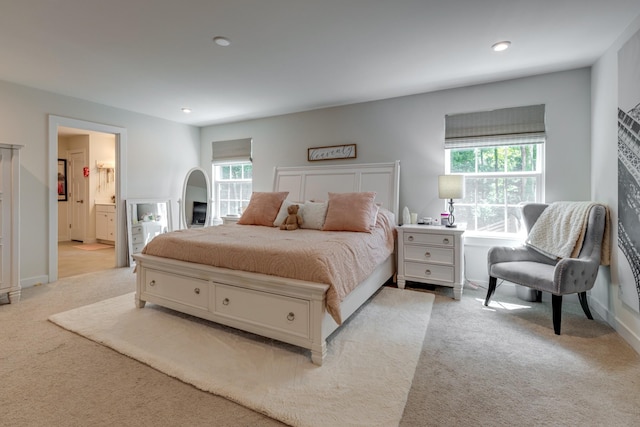 bedroom with multiple windows, connected bathroom, and light colored carpet