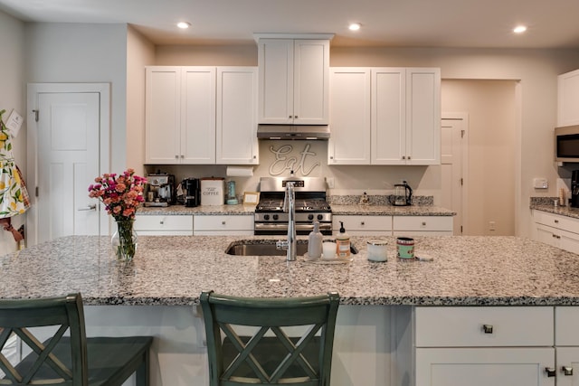 kitchen with appliances with stainless steel finishes, white cabinetry, a kitchen breakfast bar, a spacious island, and light stone countertops