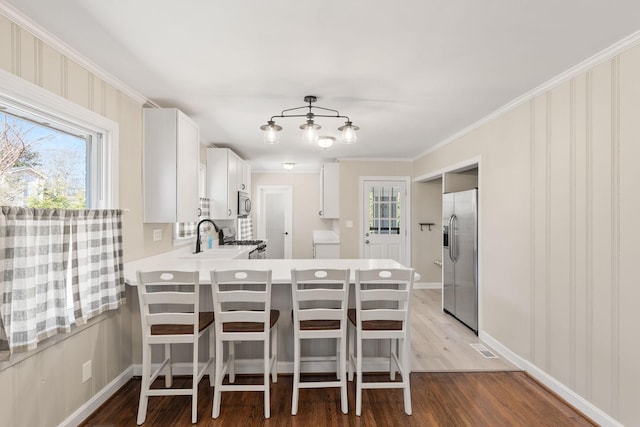 kitchen with a kitchen bar, white cabinetry, light wood-type flooring, appliances with stainless steel finishes, and kitchen peninsula