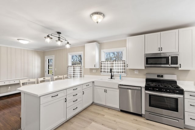 kitchen featuring sink, light hardwood / wood-style flooring, white cabinetry, stainless steel appliances, and kitchen peninsula