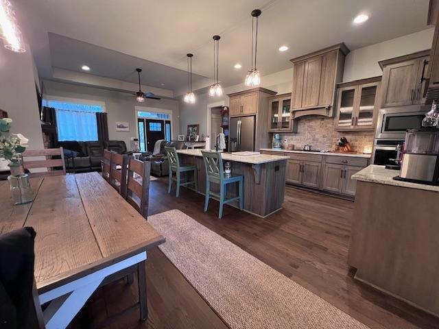 kitchen featuring pendant lighting, a breakfast bar, a kitchen island with sink, stainless steel appliances, and tasteful backsplash