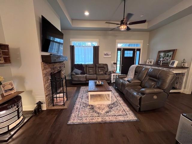 living room featuring a stone fireplace, dark hardwood / wood-style flooring, and a tray ceiling