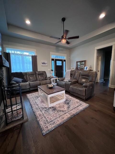 living room with a tray ceiling, dark wood-type flooring, and ceiling fan