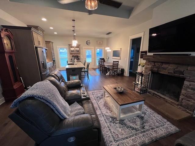 living room with dark hardwood / wood-style flooring, a stone fireplace, and ceiling fan