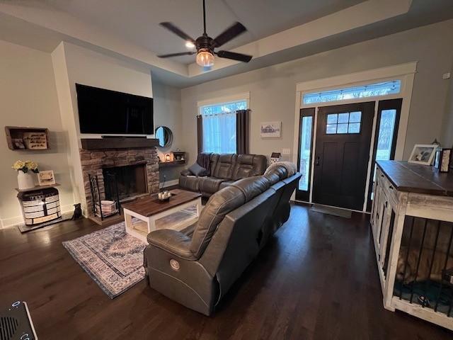 living room featuring a stone fireplace, dark hardwood / wood-style floors, ceiling fan, and a tray ceiling