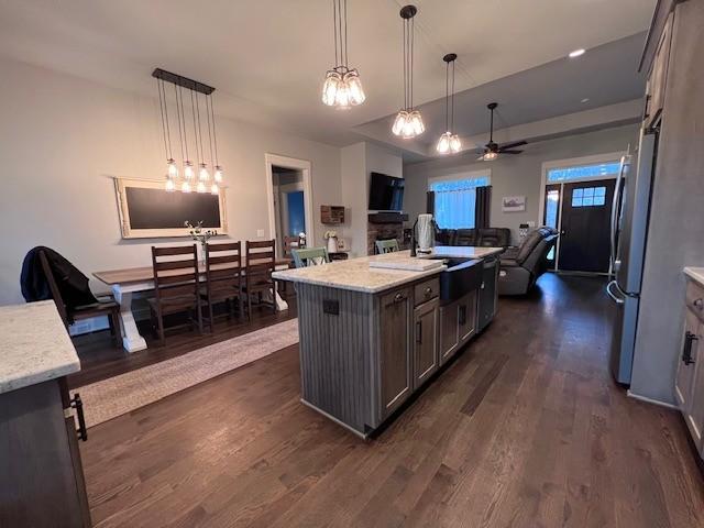 kitchen with stainless steel fridge, hanging light fixtures, a center island, light stone counters, and dark wood-type flooring