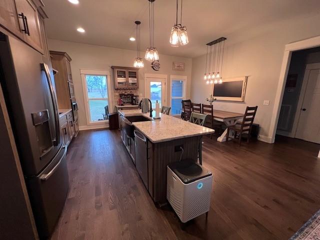 kitchen with pendant lighting, dark hardwood / wood-style flooring, stainless steel appliances, and an island with sink