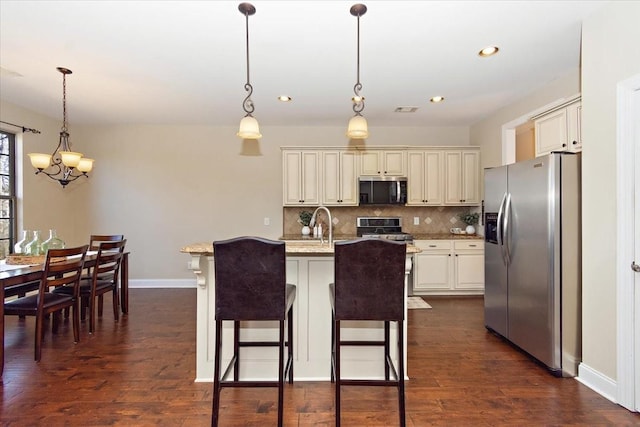 kitchen featuring pendant lighting, stainless steel appliances, a kitchen breakfast bar, and an island with sink