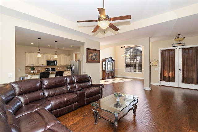 living room with dark hardwood / wood-style flooring, sink, a tray ceiling, and ceiling fan