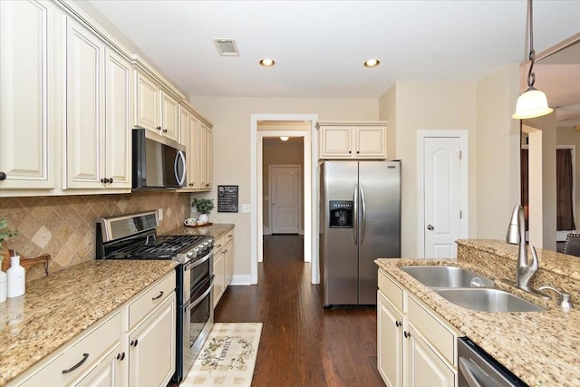 kitchen featuring sink, light stone counters, decorative light fixtures, appliances with stainless steel finishes, and cream cabinets