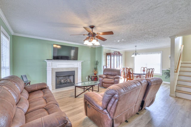 living room with ceiling fan, ornamental molding, a tiled fireplace, and light hardwood / wood-style flooring