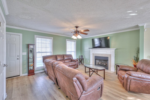 living room with crown molding, a tile fireplace, ceiling fan, a textured ceiling, and light wood-type flooring