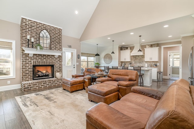 living room with wood-type flooring, high vaulted ceiling, ornamental molding, and a fireplace