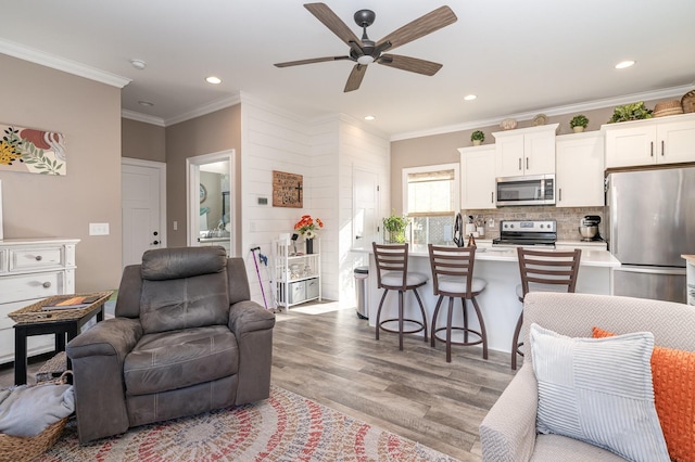 living room featuring ornamental molding, ceiling fan, and light wood-type flooring