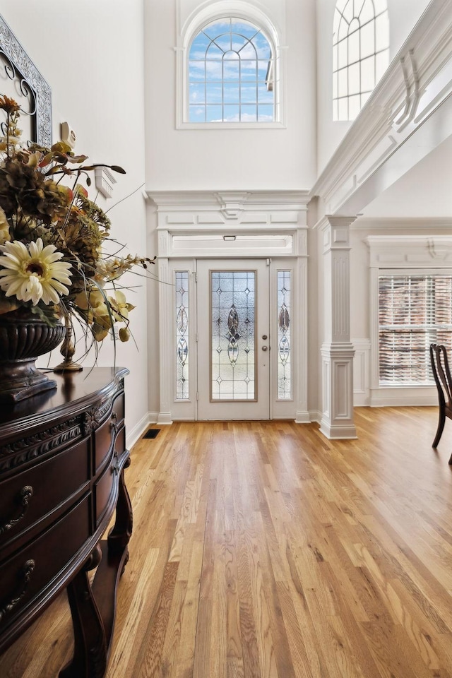 foyer entrance with light hardwood / wood-style flooring, decorative columns, and a high ceiling