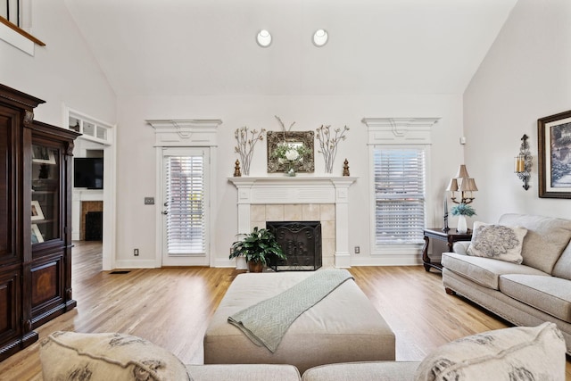 living room with high vaulted ceiling, a tile fireplace, and light hardwood / wood-style flooring