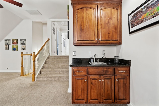 bar with sink, ceiling fan, vaulted ceiling, light colored carpet, and dark stone counters