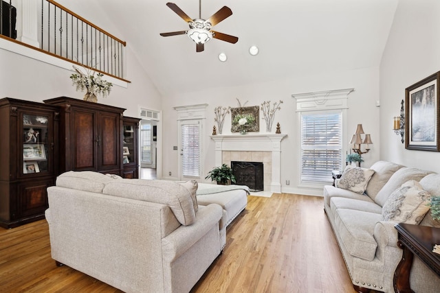 living room featuring ceiling fan, high vaulted ceiling, a tiled fireplace, and light hardwood / wood-style floors