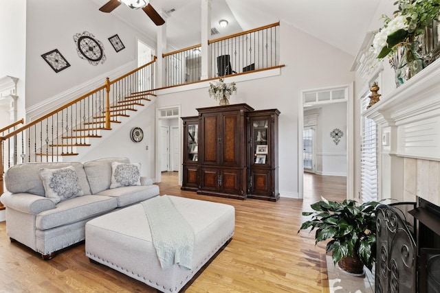 living room featuring high vaulted ceiling, light hardwood / wood-style floors, a tile fireplace, and ceiling fan