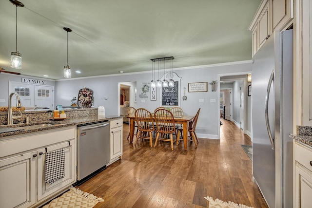 kitchen featuring appliances with stainless steel finishes, dark hardwood / wood-style floors, sink, dark stone counters, and hanging light fixtures