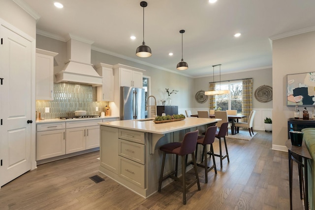 kitchen featuring custom exhaust hood, white cabinetry, a center island with sink, a kitchen breakfast bar, and stainless steel appliances