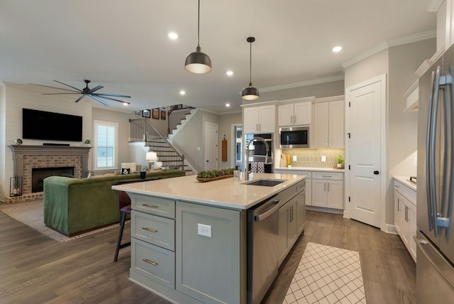 kitchen featuring appliances with stainless steel finishes, decorative light fixtures, a kitchen island with sink, and white cabinets