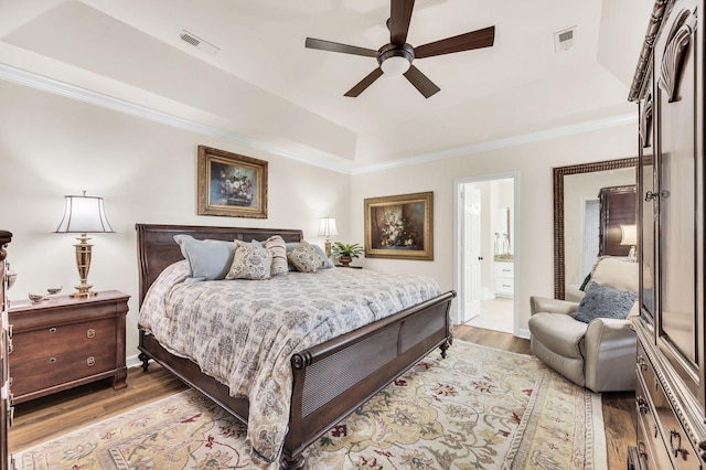 bedroom with ensuite bathroom, ceiling fan, a raised ceiling, crown molding, and light wood-type flooring