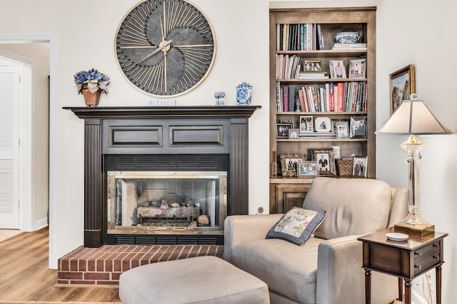 living area featuring a brick fireplace, built in shelves, and light wood-type flooring