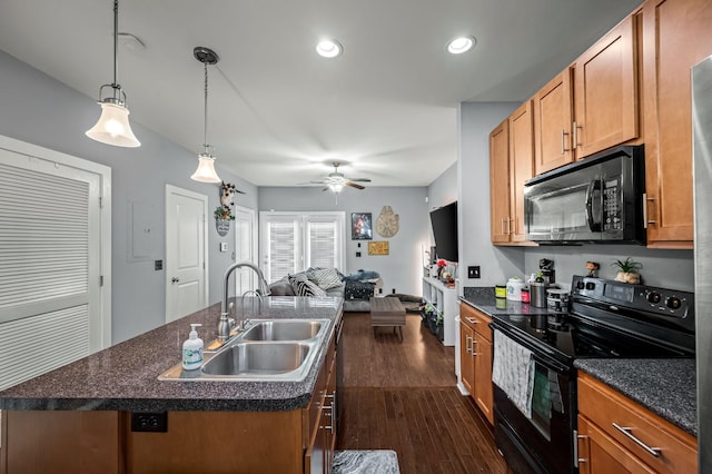 kitchen featuring dark hardwood / wood-style floors, sink, hanging light fixtures, black appliances, and a center island with sink