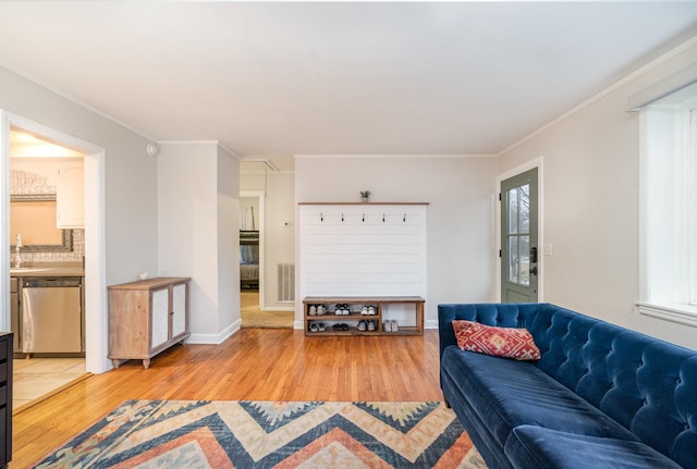 living room with ornamental molding, sink, and light wood-type flooring