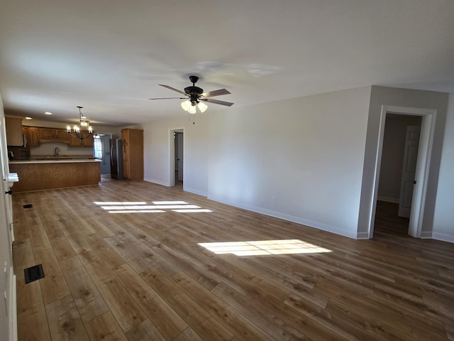 unfurnished living room featuring sink, ceiling fan with notable chandelier, and light hardwood / wood-style flooring