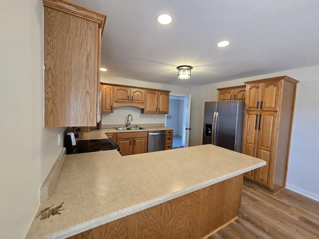 kitchen with stainless steel appliances, sink, light hardwood / wood-style floors, and kitchen peninsula