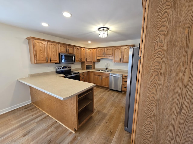 kitchen featuring stainless steel appliances, kitchen peninsula, sink, and light wood-type flooring