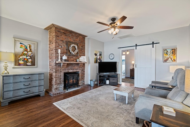 living room featuring ceiling fan, a barn door, dark hardwood / wood-style flooring, and a wood stove