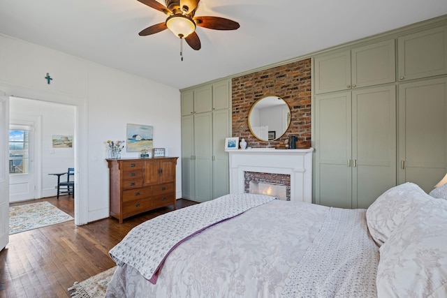 bedroom with ceiling fan, a brick fireplace, and dark hardwood / wood-style flooring