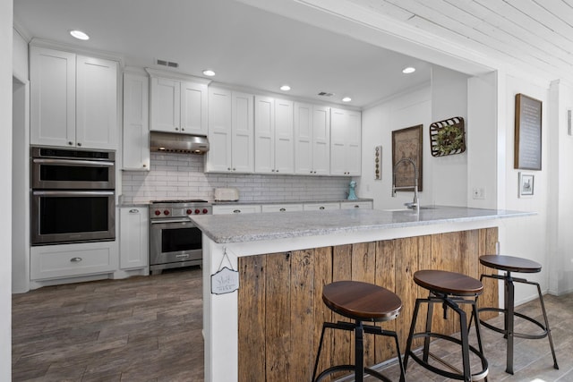 kitchen featuring sink, appliances with stainless steel finishes, a kitchen breakfast bar, decorative backsplash, and white cabinets