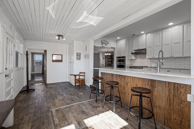 kitchen featuring dark wood-type flooring, a kitchen bar, white cabinetry, kitchen peninsula, and decorative backsplash