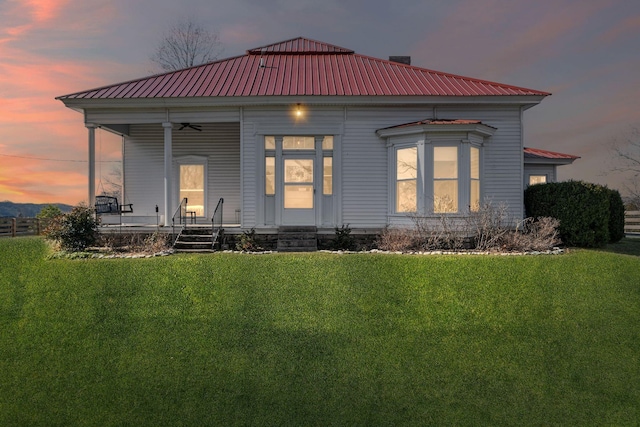 back house at dusk featuring a yard and a porch