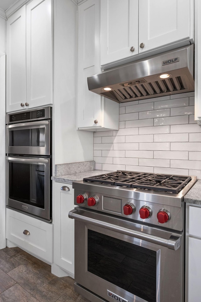 kitchen featuring appliances with stainless steel finishes, white cabinetry, backsplash, light stone counters, and ventilation hood