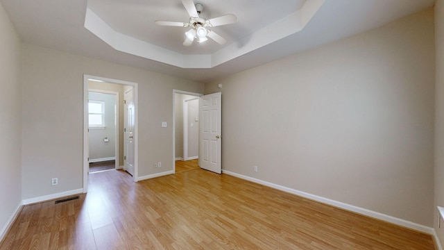 unfurnished bedroom featuring ceiling fan, connected bathroom, light wood-type flooring, and a tray ceiling