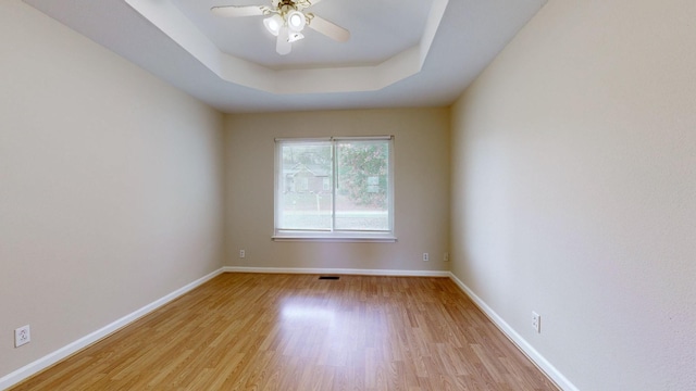 unfurnished room featuring a raised ceiling, ceiling fan, and light hardwood / wood-style floors