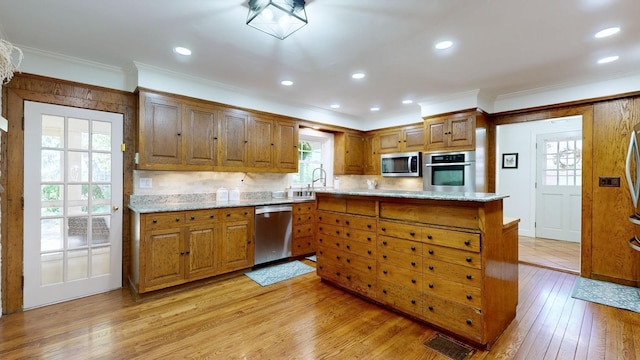 kitchen with ornamental molding, light stone counters, kitchen peninsula, stainless steel appliances, and light wood-type flooring